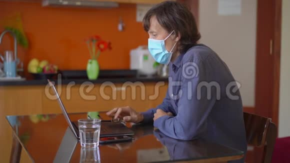 一个戴着面罩的年轻人在冠状病毒自我隔离期间在家工作镜头显示他在他的视频的预览图