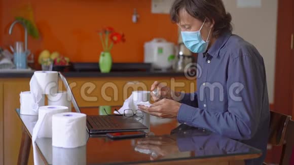 一个戴着面罩的年轻人在冠状病毒自我隔离期间坐在家里他用酒精消毒器视频的预览图