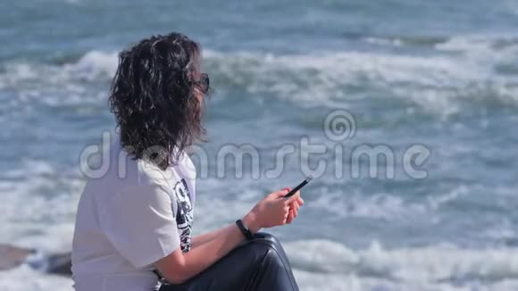 女人在海滩上放松和享受夏天的早晨拿着她的智能手机视频的预览图