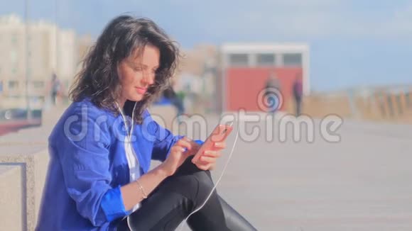 快乐微笑的年轻女人带着耳机使用手机视频的预览图