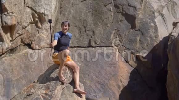 一个年轻人坐在悬崖边拍自拍视频视频的预览图