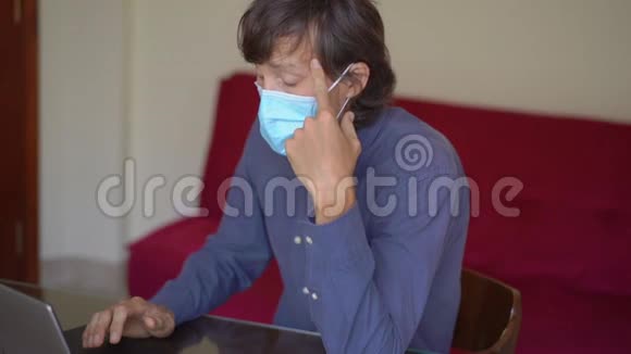 一个戴着面罩的年轻人在冠状病毒自我隔离期间在家工作他厌倦了呆在家里视频的预览图