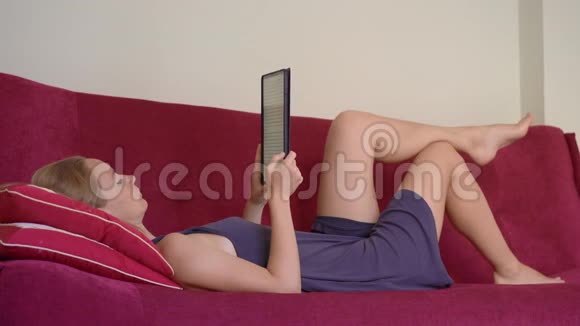 一个年轻的女人躺在沙发上看书她在冠状病毒自我隔离期间呆在家里视频的预览图