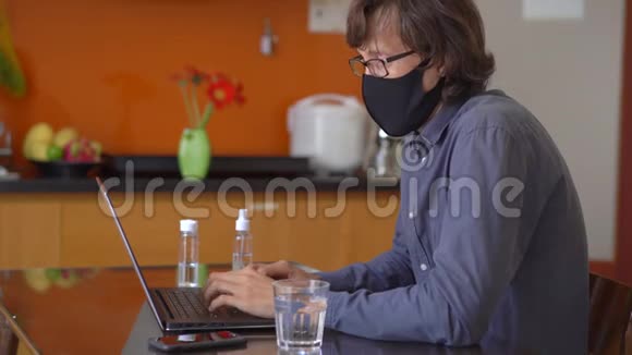 一个戴着面罩的年轻人在家中工作进行电晕病毒自我隔离视频的预览图