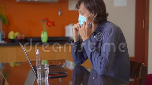 一个戴着面罩的年轻人在冠状病毒自我隔离期间在家工作慢镜头视频的预览图