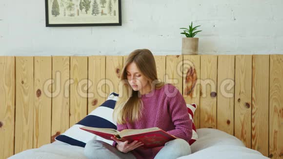 年轻漂亮的学生在床上看书远程学习视频的预览图