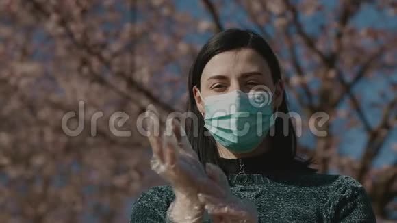 美丽悲伤的年轻女子双手戴着塑料透明手套矫正手术面罩站在樱花视频的预览图