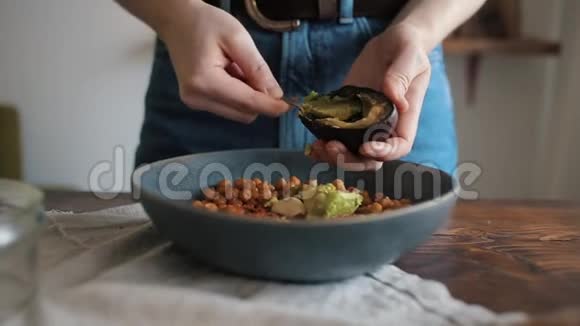 一个年轻的女孩在碗里加入鳄梨和鹰嘴豆在家里做传统的鹰嘴豆特写视频的预览图