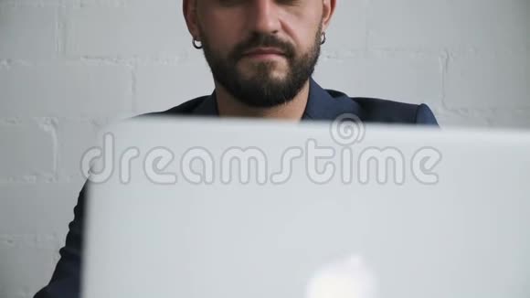 戴着耳环的长胡子帅哥在笔记本电脑上工作视频的预览图