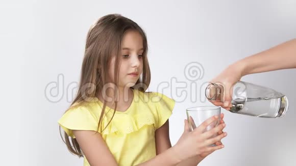 妈妈把水倒进一个小女孩杯子里小女孩把水倒进玻璃杯里一个穿着白色黄色裙子的女孩视频的预览图
