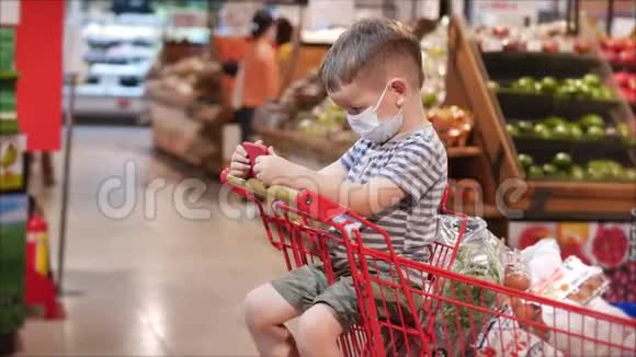 一家人在超市购物一个戴着防病毒面具的孩子坐在购物车里看电视视频的预览图