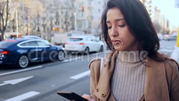 漂亮的年轻女人在路边等人接电话时用手机发短信视频的预览图