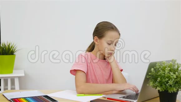 严肃的女学生坐在桌旁拿着笔记本电脑和课本做作业在家学习视频的预览图
