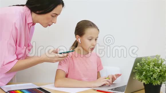 小女孩坐在桌上拿着笔记本电脑和课本做作业而年轻的母亲则帮助她视频的预览图
