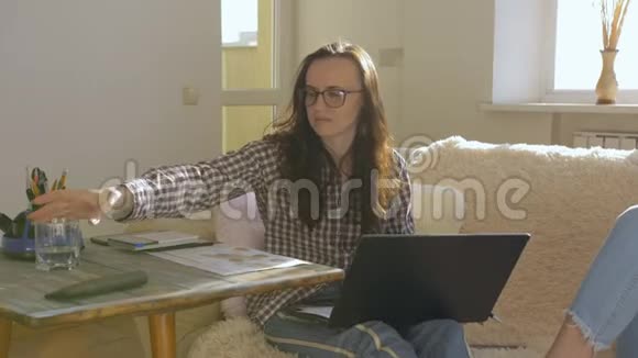一个女人在家里用笔记本电脑远程工作女人从杯子里喝水视频的预览图