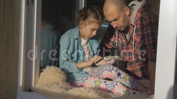 女孩坐在厨房的窗台上用智能手机告诉父亲游戏规则视频的预览图