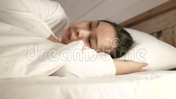 疲惫的亚洲女人在假期里躺在床上裹着一条白色的毯子视频的预览图
