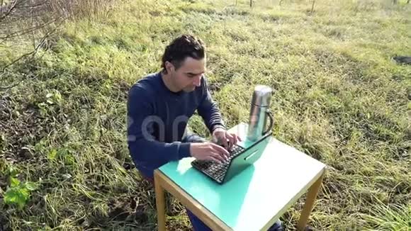 青年开发商在院子里偏远的户外工作在公园里坐着笔记本电脑和桌子有隔离概念视频的预览图