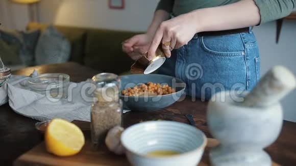 一个年轻的女孩把食材混合在一个碗里在家里煮传统的鹰嘴豆泥特写视频的预览图