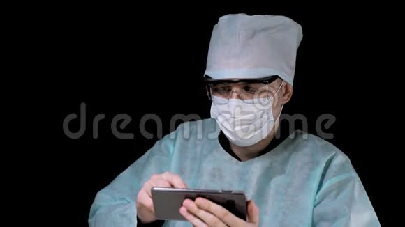 一位医生的肖像他坐在一张桌子上在黑色背景下用手机工作一位医生视频的预览图