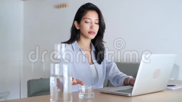 优雅的年轻商务女性在办公室用笔记本电脑工作时喝水视频的预览图