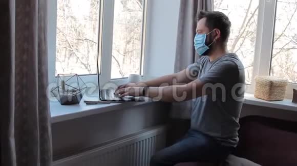 在家里用笔记本电脑工作冠状病毒在家戴防护面罩的男人视频的预览图
