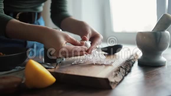 一个女孩在厨房的桌子上剥大蒜把它添加到烹饪传统鹰嘴豆泥的配料中关闭视频的预览图