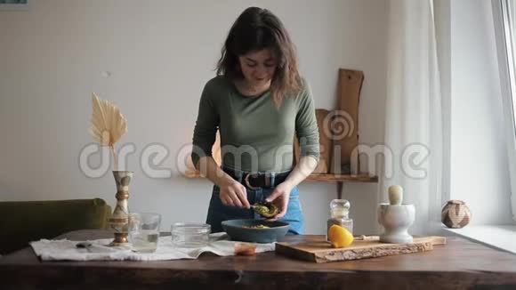 美丽的少女微笑着站在厨房的桌子旁准备自制的鹰嘴豆泥视频的预览图