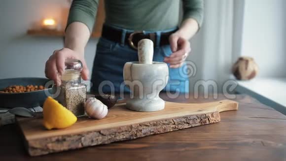 一个年轻女孩的特写镜头她的手在厨房里把香料放在灰泥里研磨加入自制的鹰嘴豆泥视频的预览图