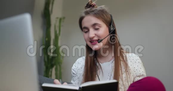 幸福的女人戴着耳机在视频会议上打招呼手提电脑坐在客厅的沙发上视频的预览图