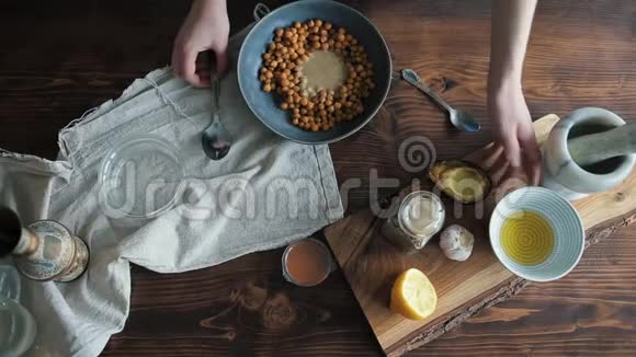 一个年轻的女孩在一个碗里加入橄榄油和鹰嘴豆以烹饪健康的传统的鹰嘴豆泥从上面看视频的预览图