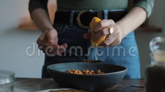 一个年轻的女孩从柠檬中榨出果汁然后把它和鹰嘴豆加到碗里在家里准备鹰嘴豆泥特写视频的预览图