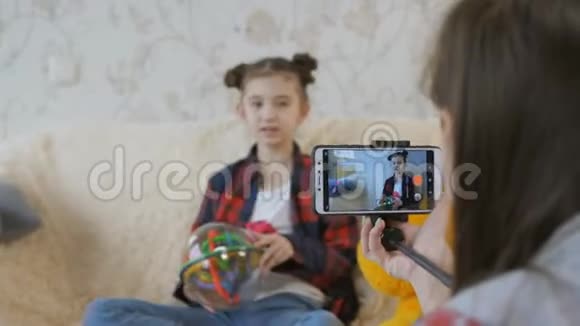 在两个姐妹的公寓里拍摄视频博客少女拍视频小妹妹在沙发上玩视频的预览图