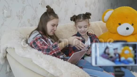 两个姐妹坐在沙发上坐在一个三脚架上用智能手机聊天为视频的预览图