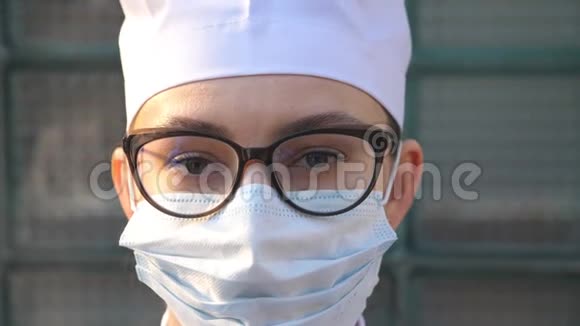 年轻女医生戴着医用口罩的肖像看着镜头戴防护面罩的医务人员视频的预览图