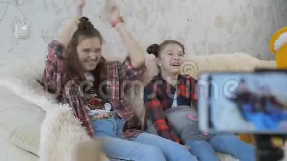 两个姐妹在智能手机拍摄视频前玩得很开心在家里智能手机上拍摄一个孩子的视频博客视频的预览图