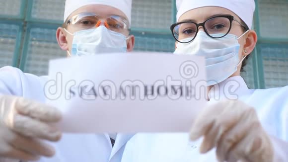 男性和女性医生正拿着一张照片上面写着冠状病毒流行期间呆在家里的铭文医疗节目视频的预览图
