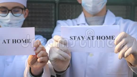在冠状病毒流行期间男医生和女医生正拿着一张铭文留在家里的照片医药视频的预览图