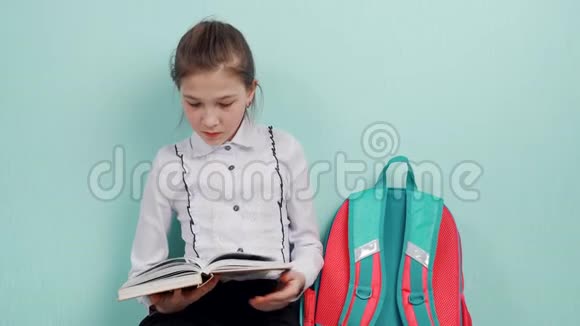 一个年轻的女学生坐在地板上靠蓝色的墙读书视频的预览图