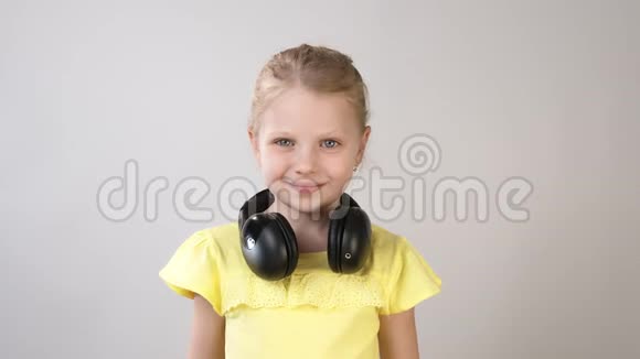 一个穿着亮黄色连衣裙的小女孩用耳机听音乐女孩把耳机放在头上视频的预览图