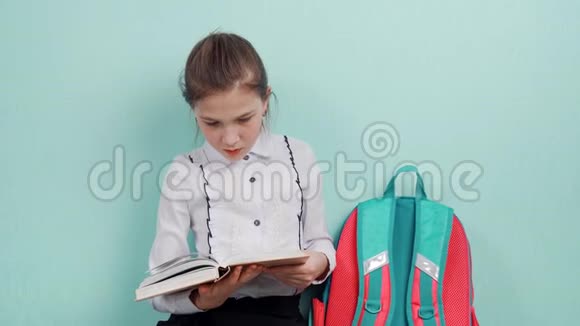 一个年轻的女学生坐在地板上靠蓝色的墙读书视频的预览图