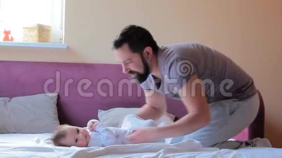年轻父亲在家给女婴换尿布和衣服视频的预览图
