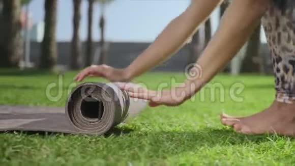 女子手在公园训练后卷起瑜伽垫女孩在草地上折叠垫子视频的预览图