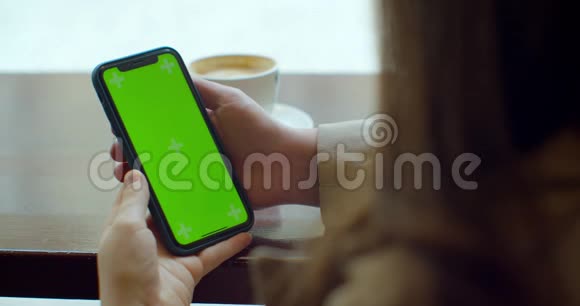 漂亮的年轻女人在咖啡馆里用她的绿色触摸屏手机视频的预览图