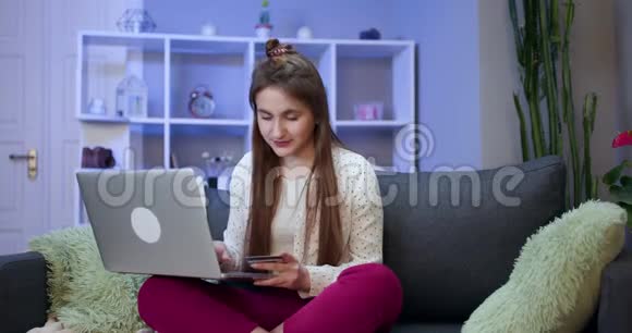女孩连接笔记本电脑并使用信用卡进行网上购物年轻女孩在网上买东西视频的预览图