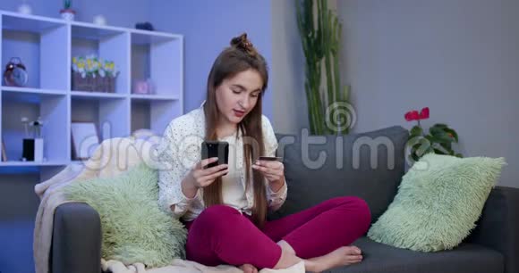 年轻女子坐在客厅的沙发上用信用卡在线购买女人用的是视频的预览图