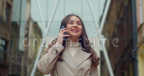 幸福的年轻女子一边走在现代化的大办公楼旁一边用手机说话快关门视频的预览图