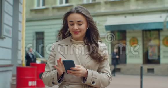 有魅力的年轻女人用电话走在老城区的街道上和朋友聊天在户外用手机的女孩视频的预览图