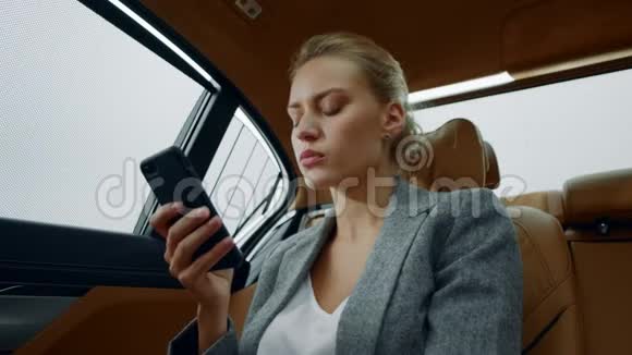 坐在电话后座的肖像女人女性在汽车上使用智能手机视频的预览图