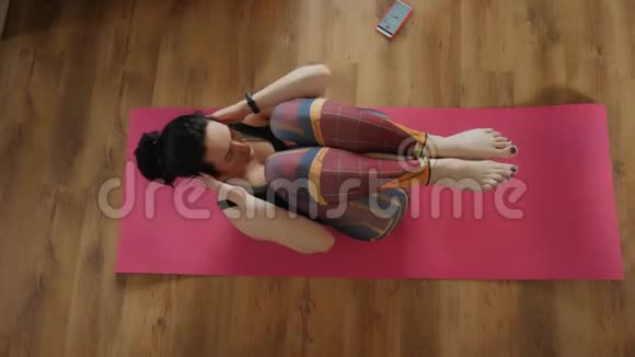 运动的女人正在做腹肌练习在家里的地板上顶部的视图穿着运动服的女运动员正在为视频的预览图